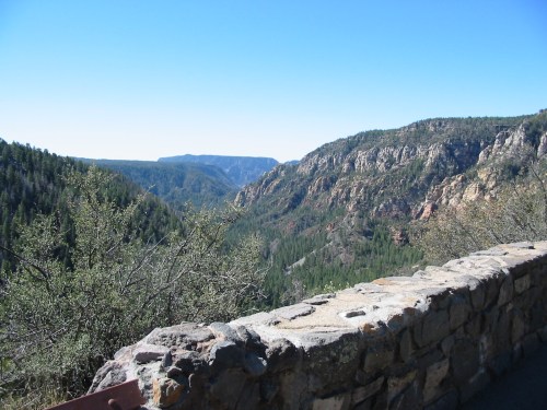 A scenic view of a canyon with lush green trees and rocky cliffs under a clear blue sky.