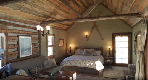 Cozy rustic bedroom with wooden beams, a large bed, and vintage skis on the wall, featuring warm lighting and a welcoming atmosphere.
