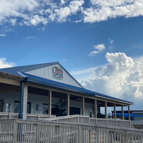 A building with a blue roof and sign, under a cloudy sky, featuring a porch and outdoor seating area.