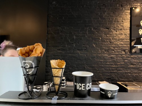 Three types of ice cream containers: a cup, a waffle cone, and a paper cone, displayed on a counter.
