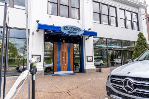 Exterior of Cuzin's Seafood restaurant featuring a blue awning, wooden double doors, and a parked Mercedes vehicle.