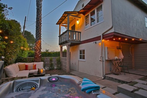 Cozy backyard with a hot tub, string lights, and a two-story house featuring a balcony and outdoor seating.