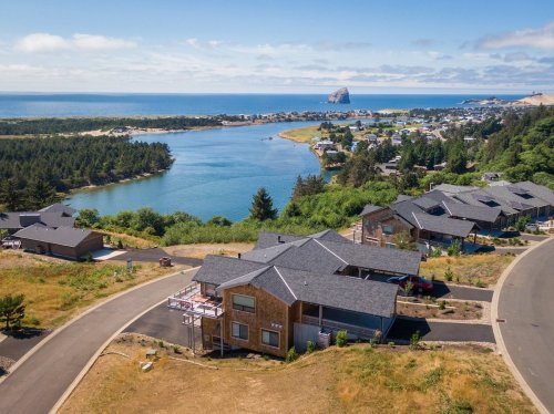 Aerial view of a coastal area with homes, a river, and a rocky outcrop in the distance under a clear blue sky.