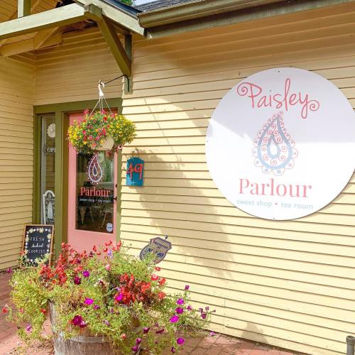 Exterior of Paisley Parlour, a sweet shop and tea room, featuring a sign, hanging flowers, and colorful flower pots.