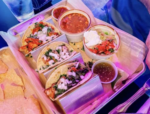 A tray with three tacos topped with onions and cilantro, a bowl of beans, salsa, and a side of tortilla chips.
