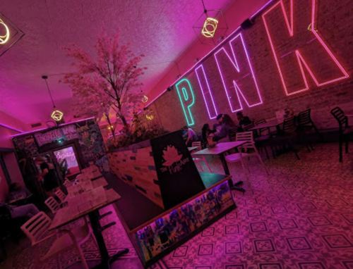 A vibrant restaurant interior with pink neon lights, colorful decor, and a lively atmosphere.