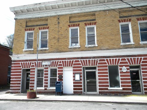 A historic brick building with a striped facade, featuring large windows and a mailbox outside.