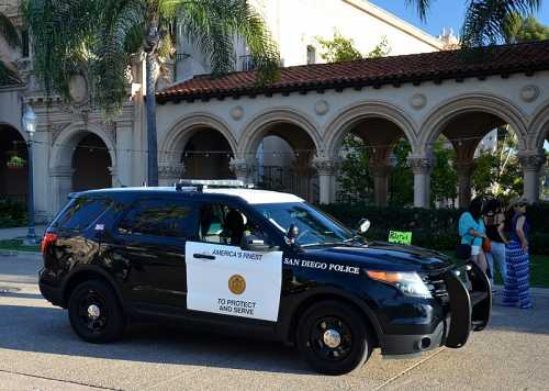 A San Diego police SUV parked near a historic building with palm trees in the background.