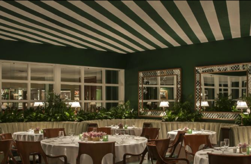 Elegant restaurant interior with green walls, striped ceiling, and stylish seating, adorned with plants and mirrors.