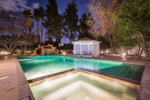 A serene pool area at night, featuring a gazebo, palm trees, and a water slide, illuminated by soft lighting.