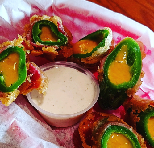 A basket of crispy jalapeño poppers filled with cheese, served with a side of creamy dipping sauce.