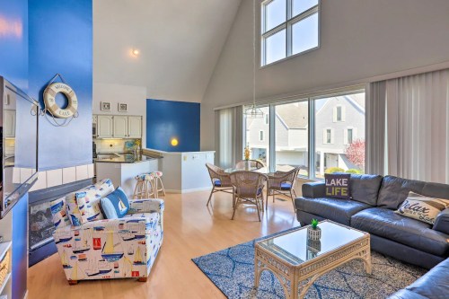 Bright living area with large windows, blue walls, a cozy sofa, and a dining space overlooking a lake.