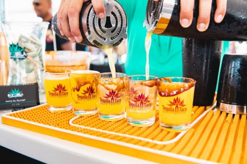 A bartender pours drinks into shot glasses at a vibrant event featuring tequila and tacos.