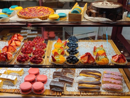 A display of colorful pastries, including fruit tarts, macarons, and chocolate desserts, arranged on lace doilies.