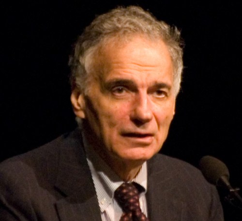 A man in a suit speaking at a microphone, with a serious expression and gray hair.