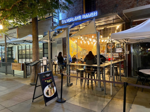 Outdoor dining area of Silverlake Ramen, featuring string lights and a vibrant mural, with patrons seated at tables.