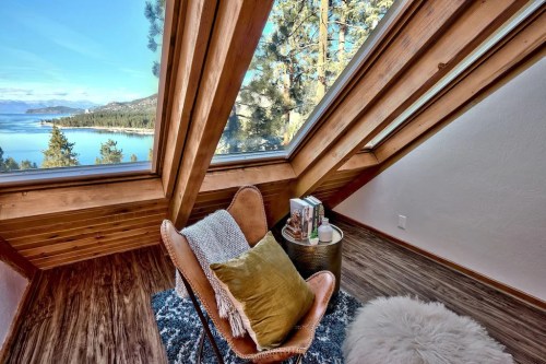 Cozy reading nook with a chair, side table, and scenic lake view through large angled windows.