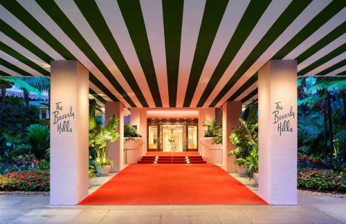 Entrance of The Beverly Hills hotel, featuring a striped green and white canopy, red carpet, and lush tropical plants.