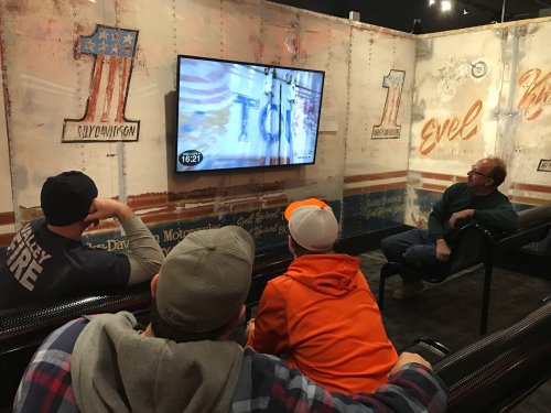 A group of four people watching a video on a screen in a rustic, themed setting.