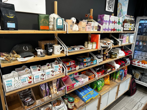 A wooden shelf filled with various snacks, drinks, and merchandise in a cozy store setting.