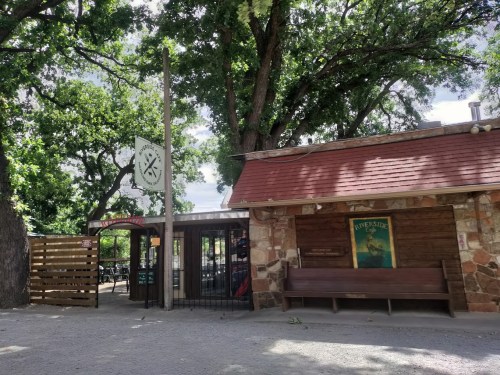 A rustic building with a stone facade, surrounded by trees, featuring a sign and a gated entrance.