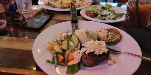 Plates of food featuring steak with crab, mashed potatoes, vegetables, and a side salad on a wooden table.