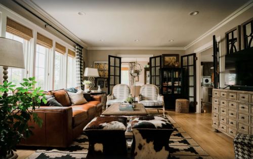 Cozy living room with leather sofa, patterned chairs, wooden coffee table, and large windows, featuring warm decor.