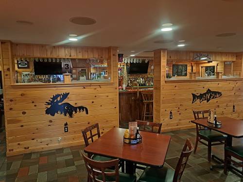 Interior of a rustic restaurant with wooden walls, bar area, and fish-themed decor. Tables are set for dining.