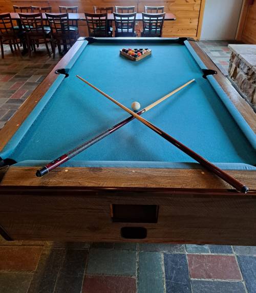 A pool table with a blue felt surface, two crossed cues, and a triangle of balls set up for a game.