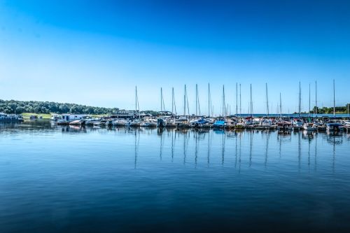A serene marina with sailboats docked, reflecting in calm water under a clear blue sky.
