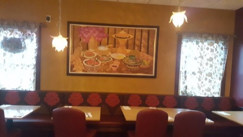 Interior of a restaurant featuring a colorful wall painting and decorative curtains, with tables and chairs set up.