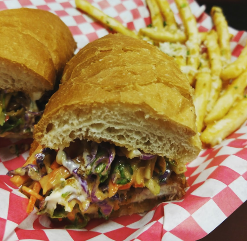 A close-up of a sandwich filled with colorful slaw, served with a side of golden fries in a red-checkered basket.