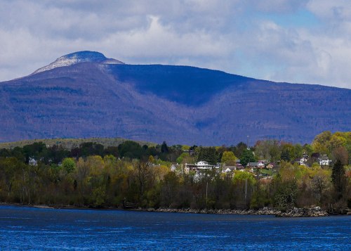 A scenic view of a mountain with a small town at its base, surrounded by lush greenery and a calm body of water.