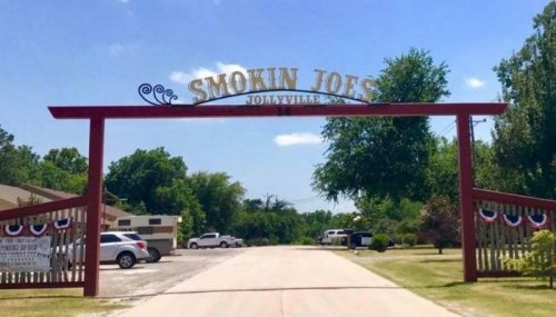 Entrance sign for Smokin' Joe's in Jollyville, framed by trees and a clear blue sky.