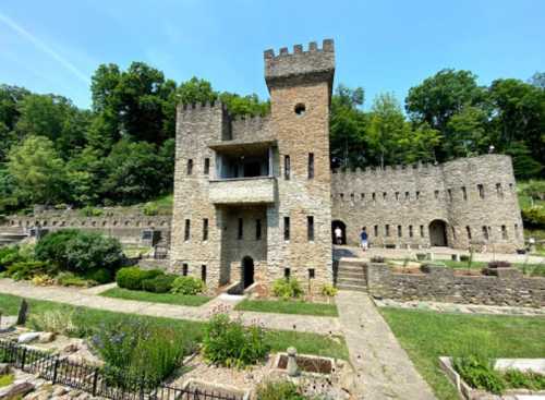 A stone castle with towers surrounded by greenery and gardens on a sunny day.