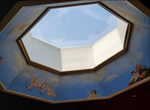 Octagonal skylight with blue sky and painted cherubs on the surrounding ceiling.