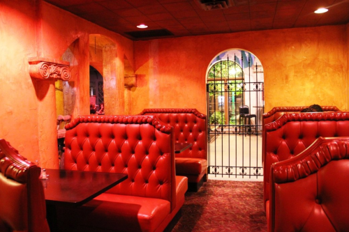 Cozy restaurant interior with red tufted booths and an arched doorway leading to a garden area. Warm orange walls.