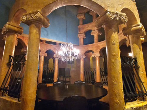 Elegant dining area featuring ornate columns, a chandelier, and a large round table in a warm, inviting setting.