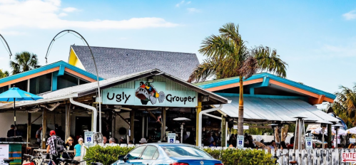 Exterior of the Ugly Grouper restaurant with colorful signage and outdoor seating under a blue sky.