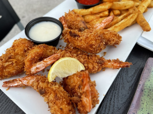 A plate of crispy fried shrimp with a lemon wedge, served with fries and dipping sauces.