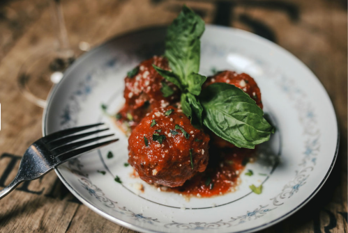 A plate of meatballs topped with marinara sauce and fresh basil, served with a fork on a rustic wooden table.