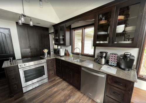 Modern kitchen with dark wood cabinets, stainless steel appliances, and a granite countertop. Bright natural light from windows.