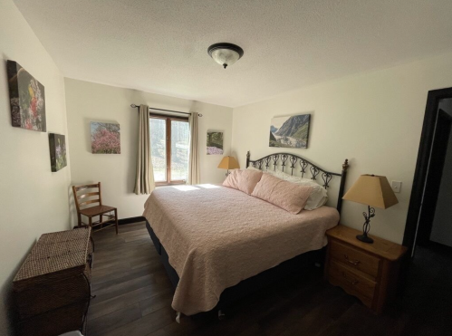 Cozy bedroom with a large bed, wooden furniture, and nature-themed artwork on the walls, illuminated by natural light.