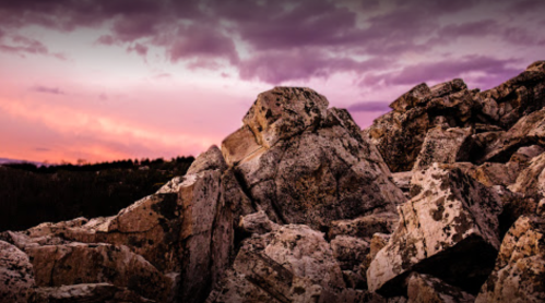 Rocky landscape under a purple and pink sky at sunset, with large boulders in the foreground.