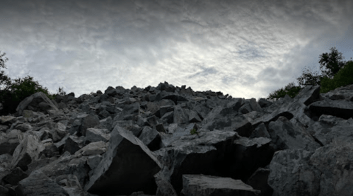 A rocky hillside under a cloudy sky, with scattered boulders and patches of greenery.