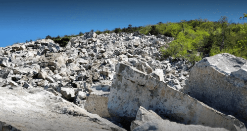 A rocky hillside covered in large boulders and scattered greenery under a clear blue sky.