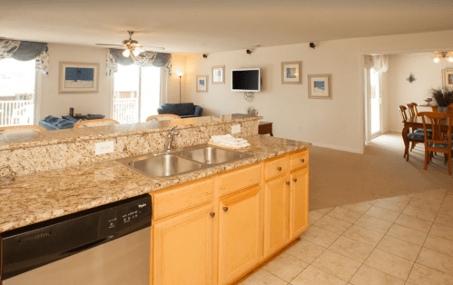 Bright, open-concept kitchen with granite countertops, dining area, and living room featuring large windows and beach decor.