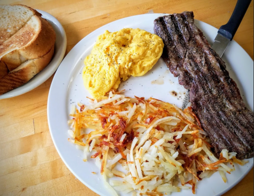 A plate with scrambled eggs, crispy hash browns, grilled steak, and a slice of toast on the side.