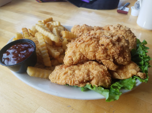 A plate of crispy fried chicken tenders on lettuce, served with crinkle-cut fries and a side of barbecue sauce.