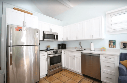 Modern kitchen with stainless steel appliances, white cabinets, and a tiled floor. Bright and airy design.